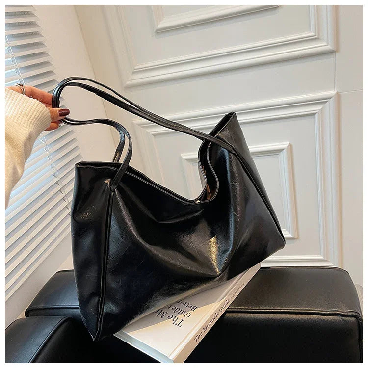 Stylish black leather tote bag for women, held by hand near window, perfect for everyday fashion and travel.